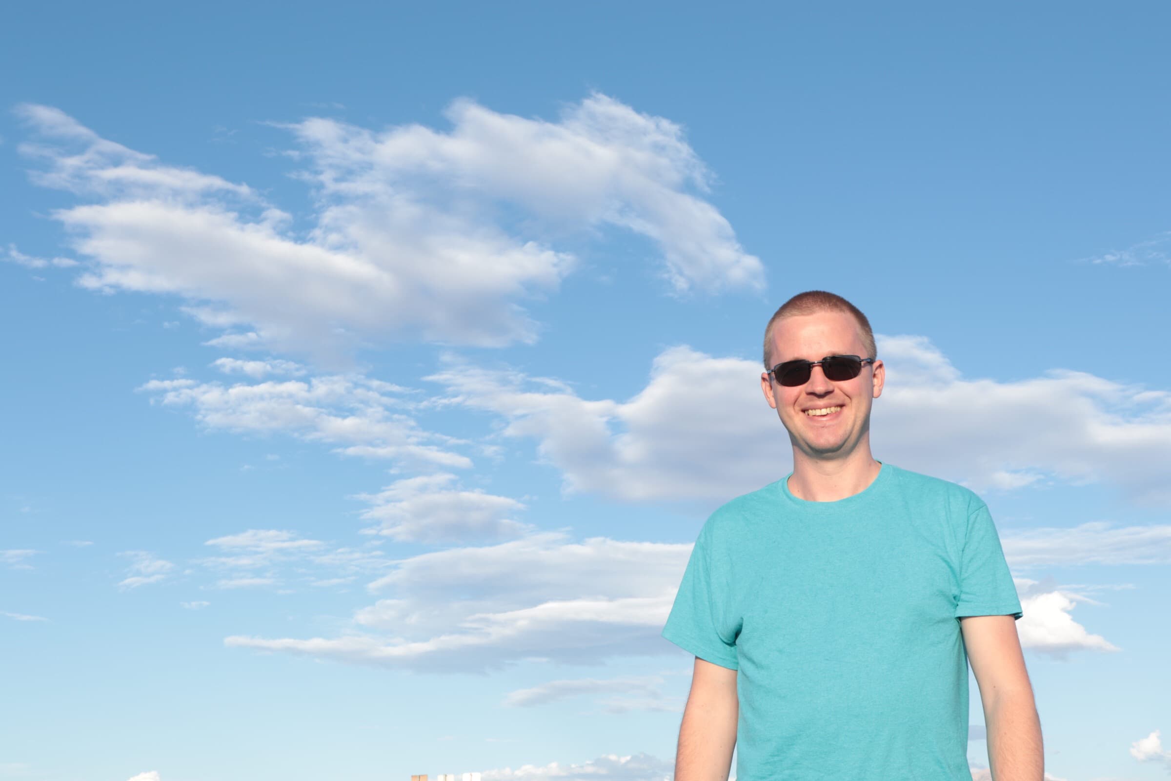 Alden Gillespy from a low angle outdoors with clouds in the sky